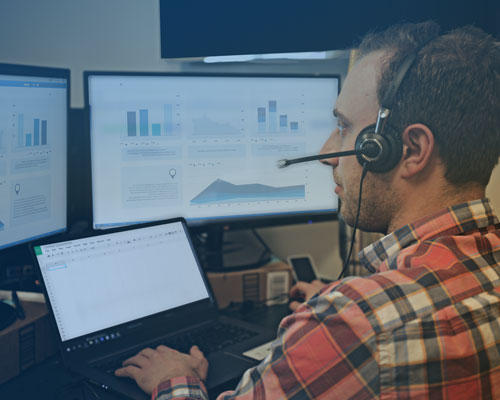 A Sherpa Auto Transport expert wearing a headset in front of two monitors.