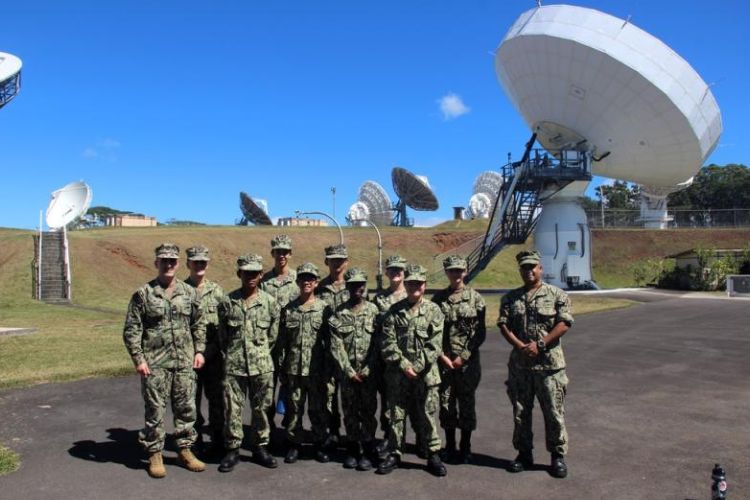 U.S. Navy personnel pose in front of satellite communication dishes at NCTAMS PAC under a clear blue sky