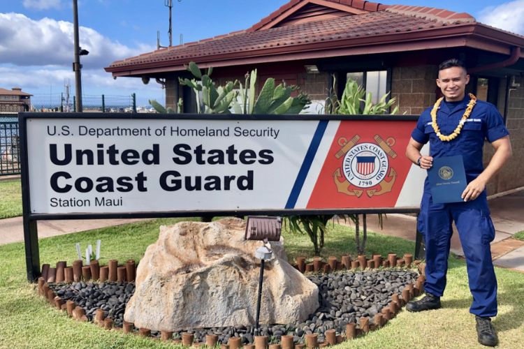 U.S. Coast Guard member at Station Maui holding a certificate, standing beside the official station sign with a lei around his neck.