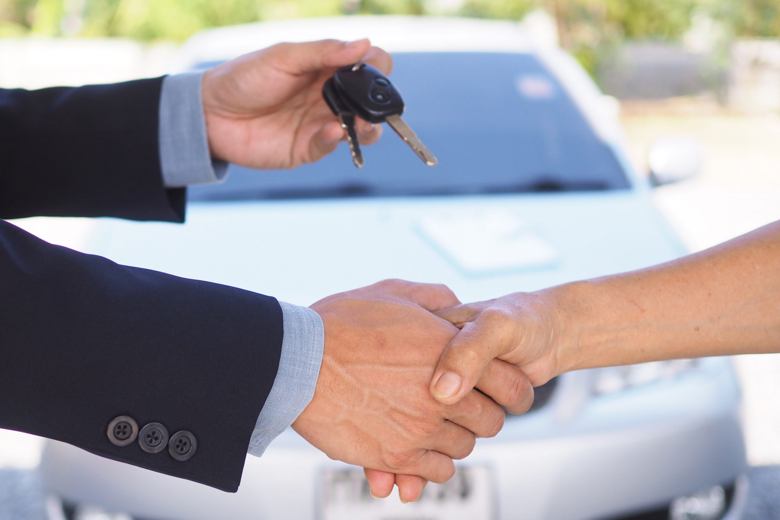 Salesman handing over a key and shaking the hand of a customer in front of a new car