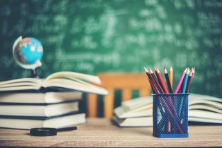 Open college textbooks and a compilation of pencils in front of a green chalkboard