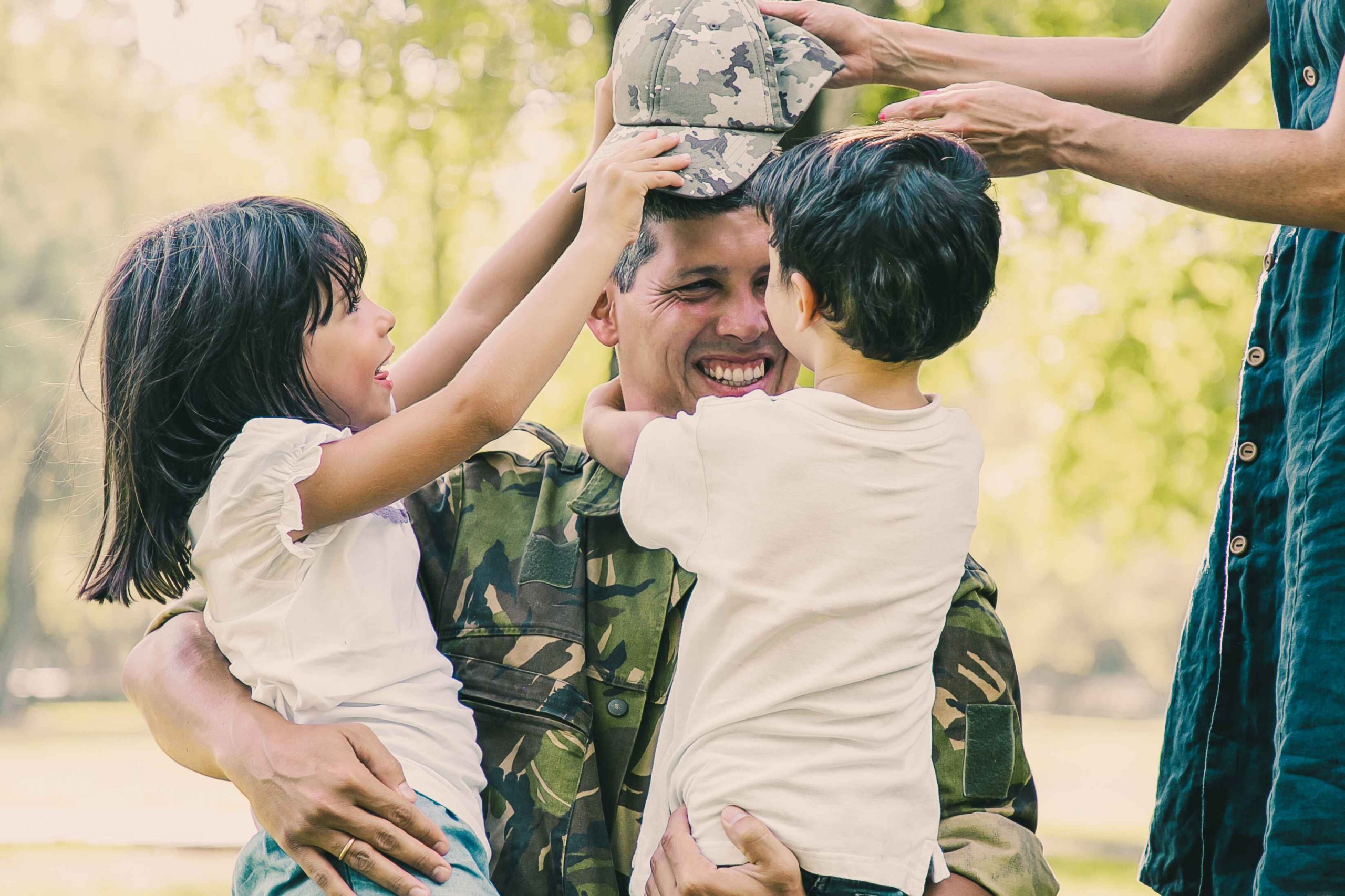 Two happy kids and their mom hugging father in military uniform outside
