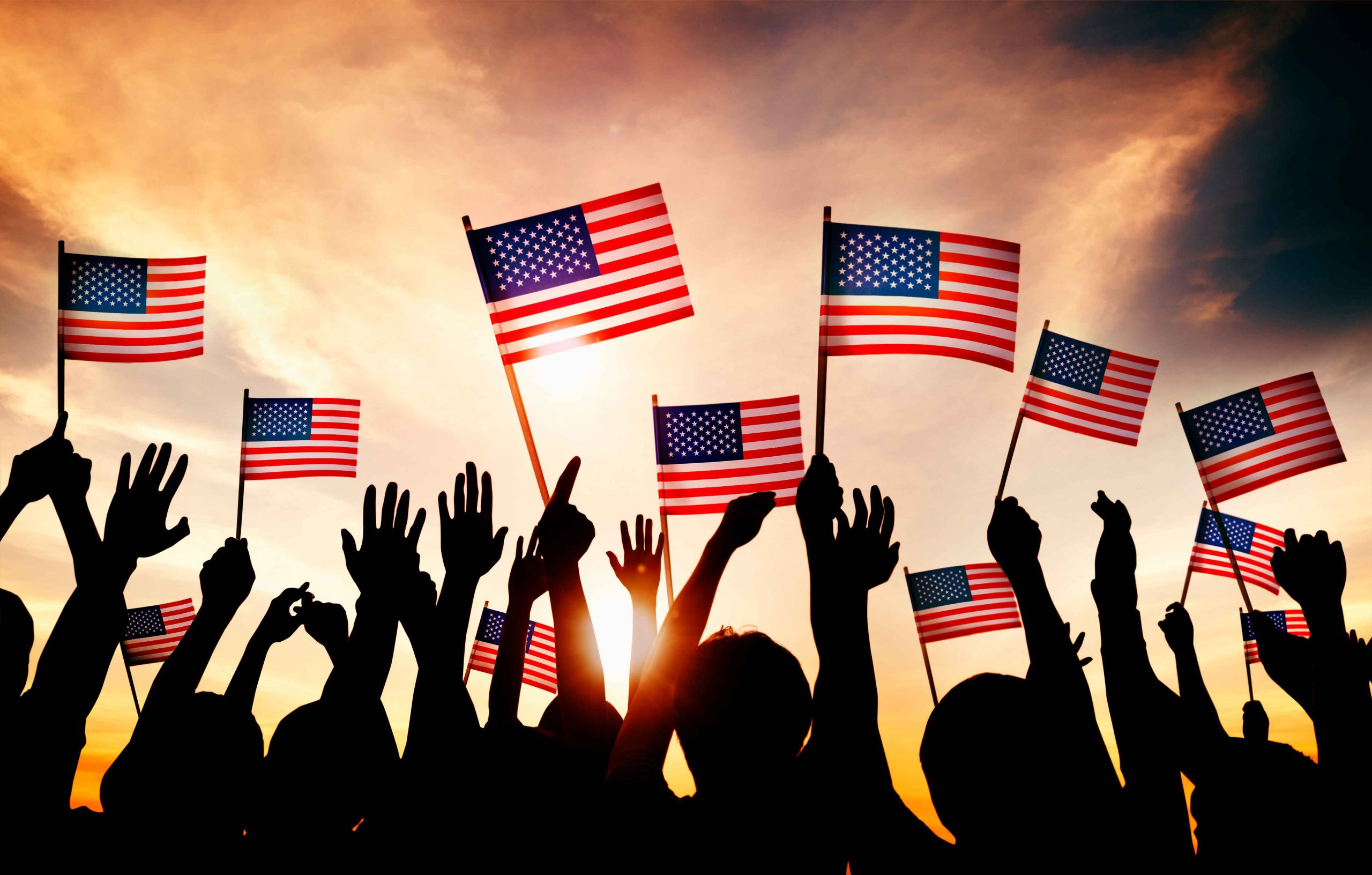Backlit photo of group of people waving American flags in the air
