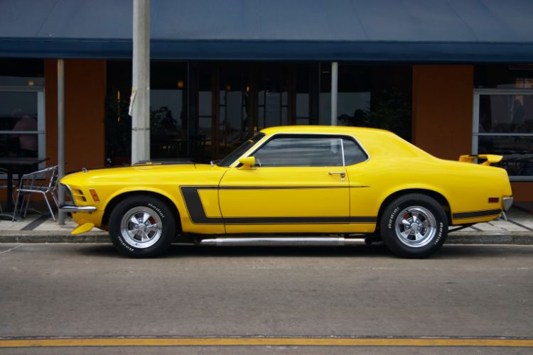 Classic yellow Ford Mustang from the 1960s-1970s parked on a city street, showcasing vintage muscle car design and performance.