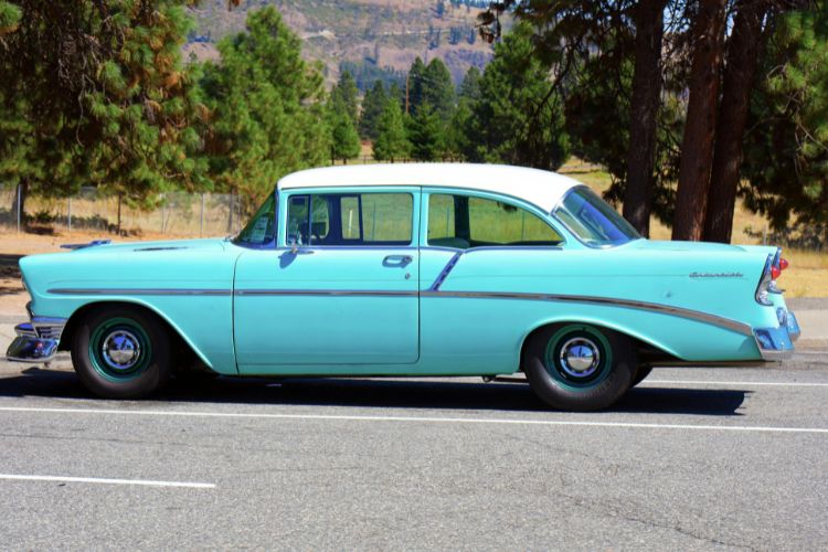 Classic turquoise Chevrolet Bel Air from the 1950s parked on a scenic road, showcasing vintage car design with chrome accents and a white roof.