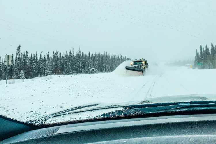 Snow plow clearing icy Alaska winter road